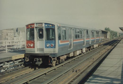 A silver, blue, and red CTA 2000-series rapid transit train on an elevated track on a clear day.