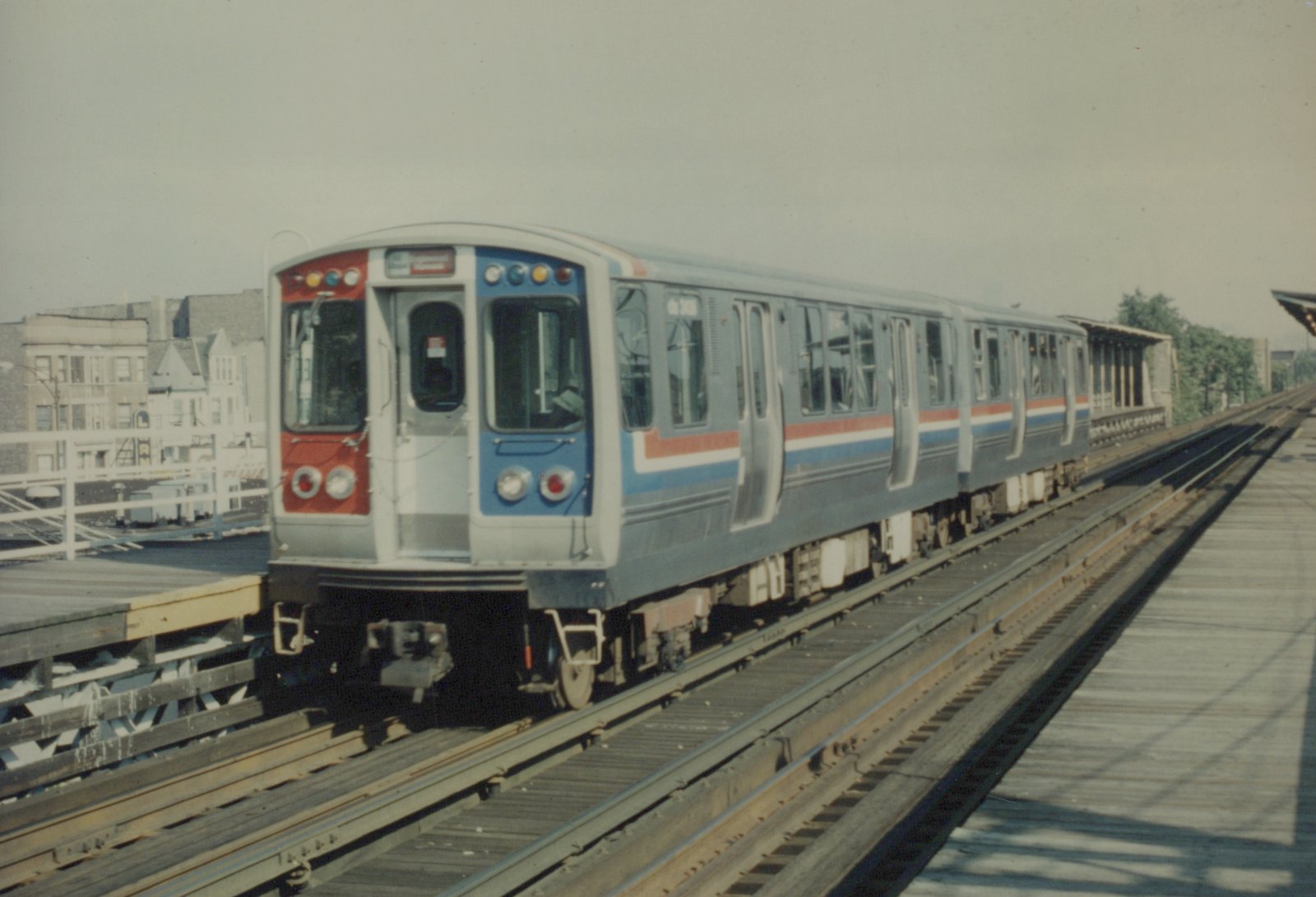 A silver, blue, and red CTA 2000-series rapid transit train on an elevated track on a clear day.