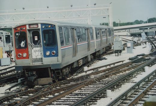 A silver Chicago Transit Authority rapid transit car with red, white, and blue stripes, number 2425, is positioned on tracks in a yard, with another car, number 514, visible in the background.