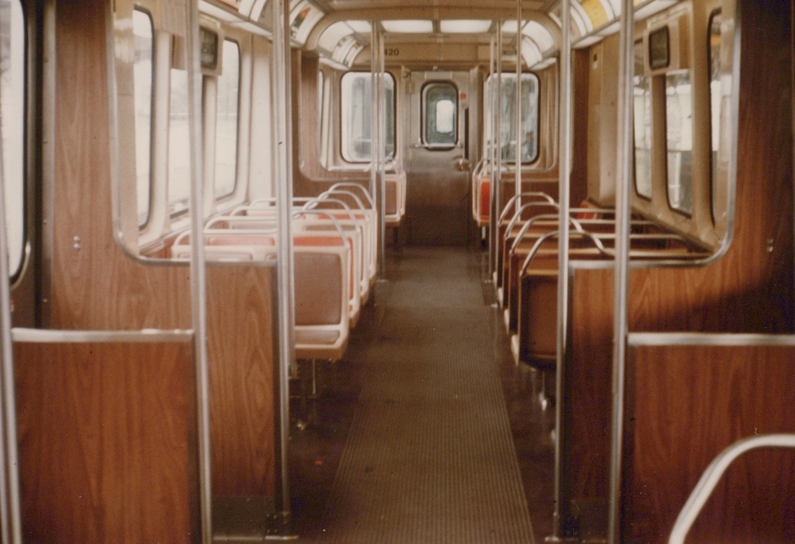 Looking down the aisle of an empty rapid transit car with wood paneling, rows of seats, and metal poles, with the number 420 visible above the far door.