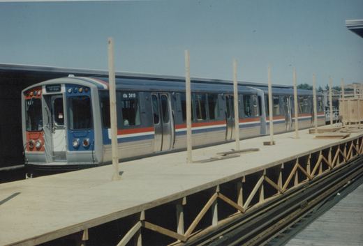 A blue and silver Chicago Transit Authority train, number 2419, labeled 'Ravenswood All stops', is stopped at a wooden platform under construction on an elevated track on a sunny day.