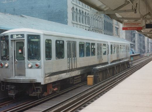 A silver Chicago Transit Authority train car, number 2275, is stopped at an elevated station platform on a cloudy day.