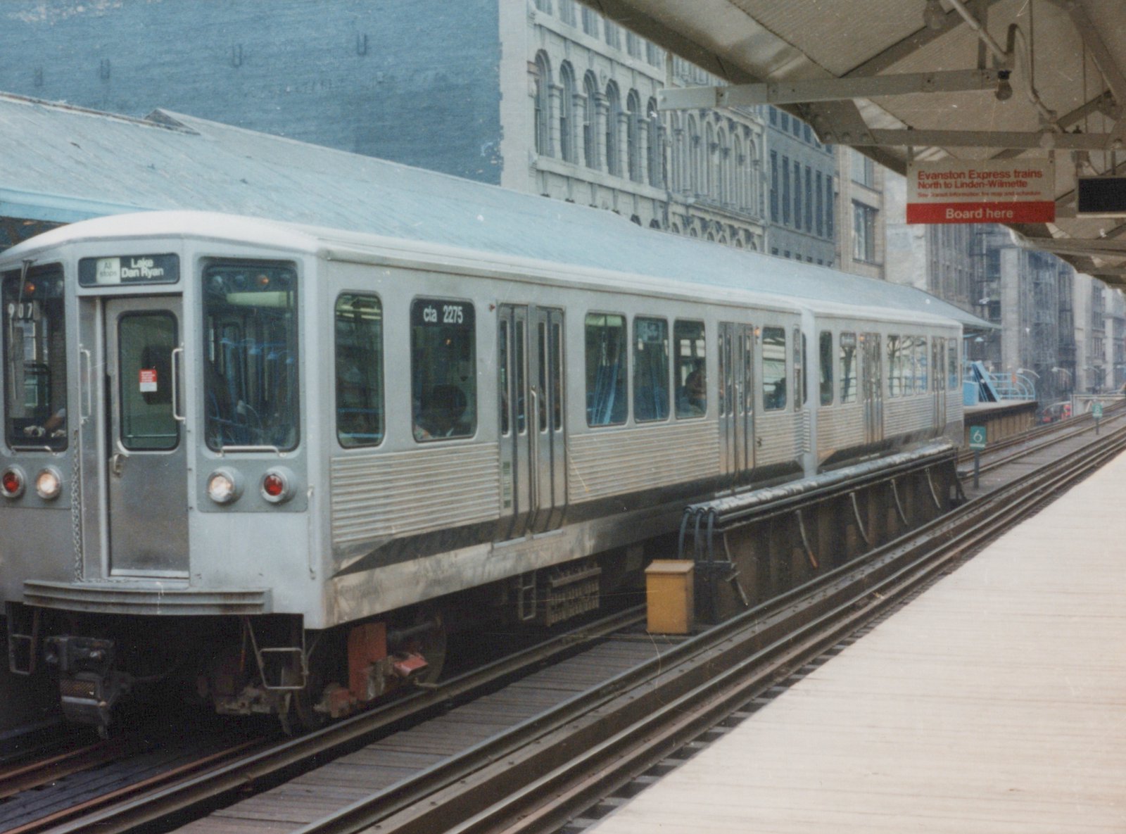 A silver Chicago Transit Authority train car, number 2275, is stopped at an elevated station platform on a cloudy day.