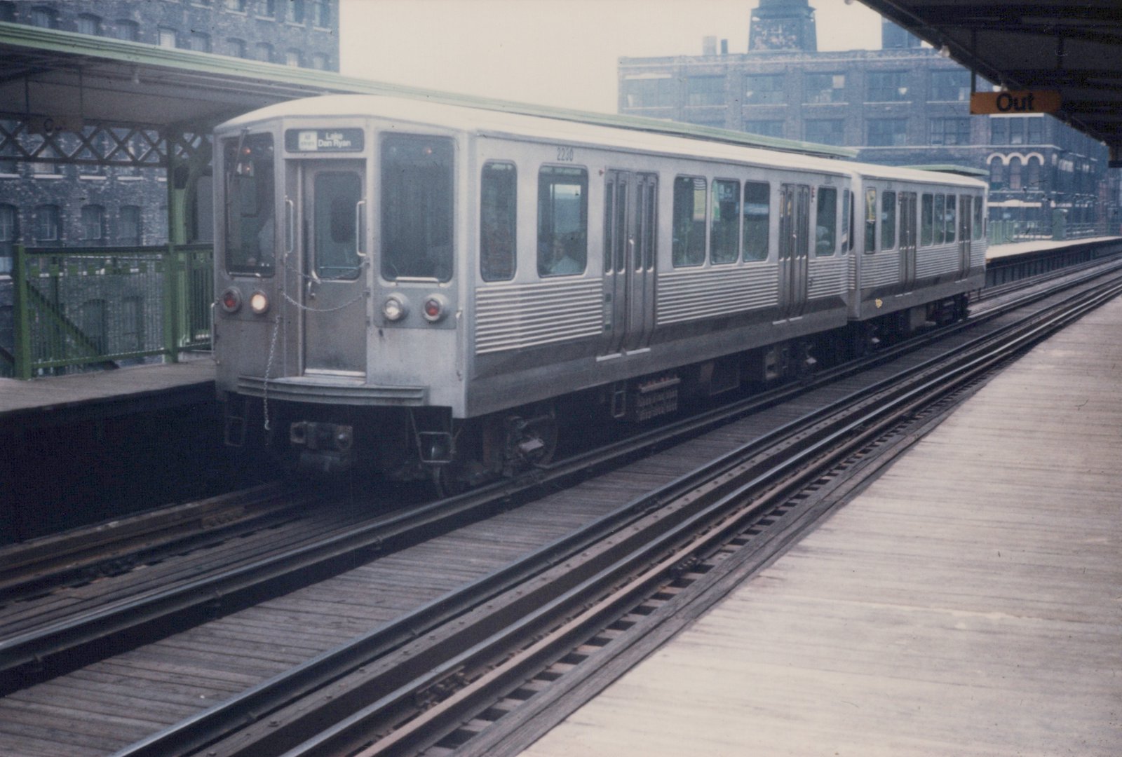 A silver Chicago Transit Authority 2200-series rapid transit car, numbered 2230, is stopped at an elevated station platform with a green roof and a 'Lake Dan Ryan' destination sign.