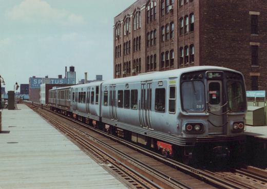 A silver CTA train with red underframe, led by car 207, on an elevated track next to a brick building.
