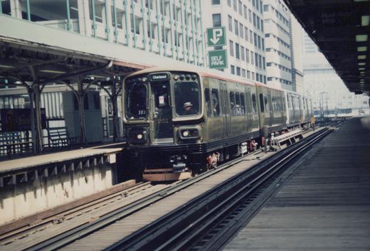 An olive green and cream Chicago Transit Authority rapid transit train, numbered 1892 and marked 'Chartered', is stopped at an elevated station platform with a 'SELF PARK' sign visible behind it.