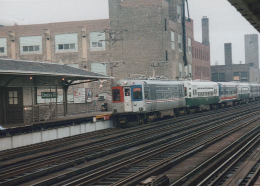 A silver, green, and red electric train with the number 41 is stopped at the Diversey elevated station, with industrial buildings in the background.