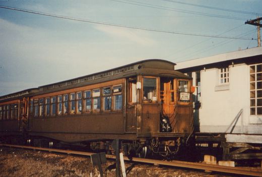 A vintage brown interurban car numbered 2817 is parked on a private right-of-way next to a white building, with a trolley pole overhead and a 'LOOP.' destination sign.
