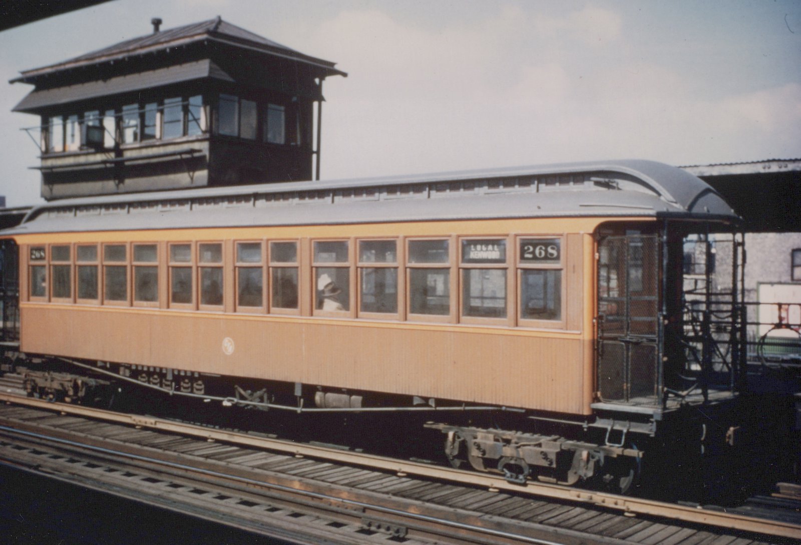 A vintage tan and cream interurban railcar with the number 268 and a 'LOCAL KENWOOD' sign, stopped on elevated tracks near a signal tower.