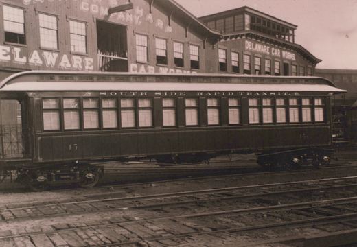 A side view of a vintage rapid transit car labeled 'South Side Rapid Transit' with the number 13, parked in front of a building with 'Delaware Car Works' lettered on it in 1892.