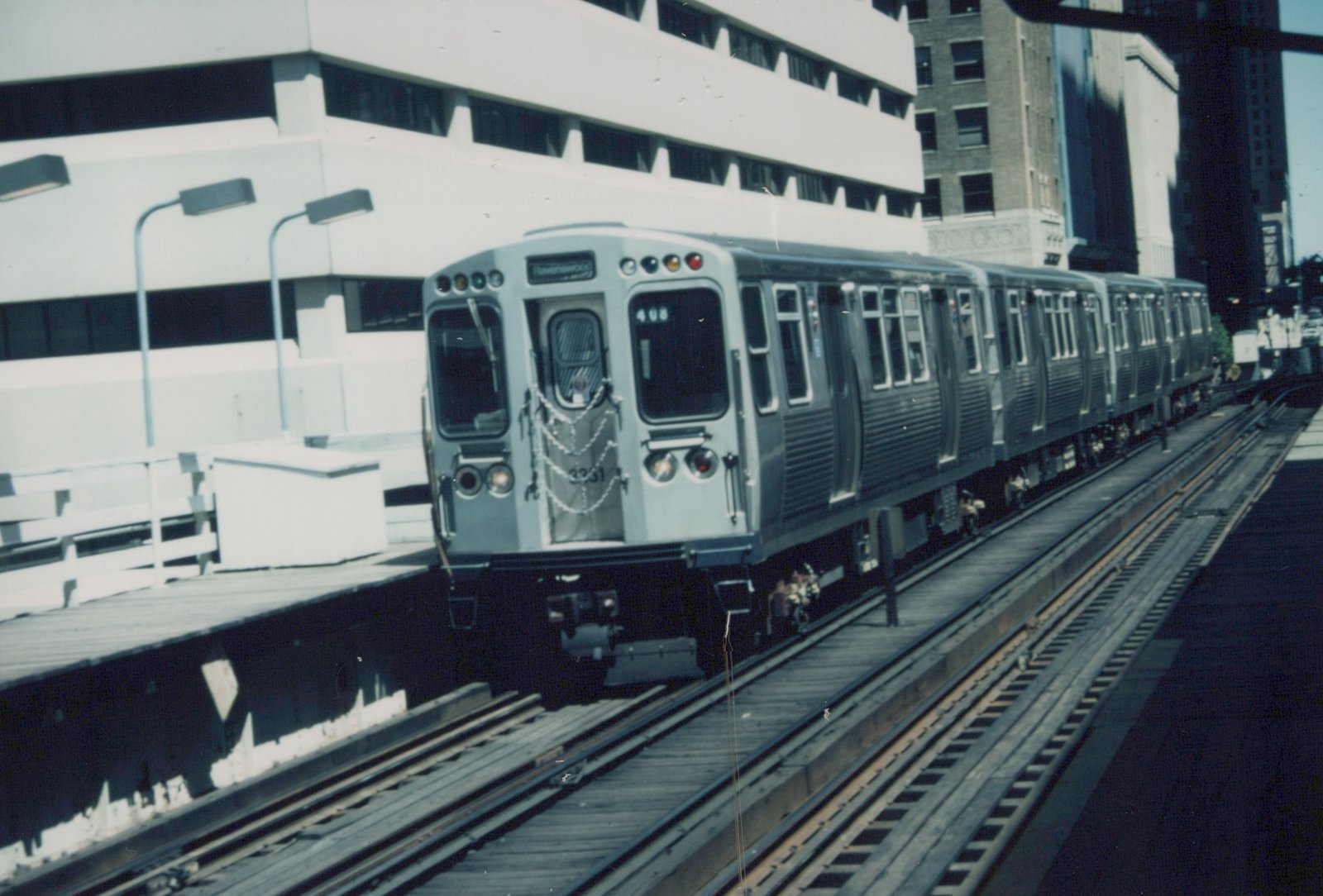 A silver CTA rapid transit train with the number 3331 and a 'Ravenswood' sign is on an elevated track next to a station platform under a clear sky.