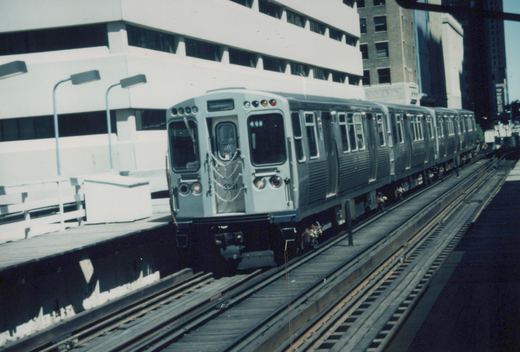 A silver CTA rapid transit train with the number 3331 and a 'Ravenswood' sign is on an elevated track next to a station platform under a clear sky.