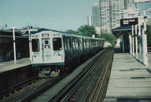 A white and blue CTA train is stopped at an outdoor elevated station with a sign that reads 'Rush hour stop'.