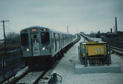 A gray Chicago 'L' train with the number 3255 on its front and a 'Midway' destination sign is moving on an elevated track under an overcast sky.