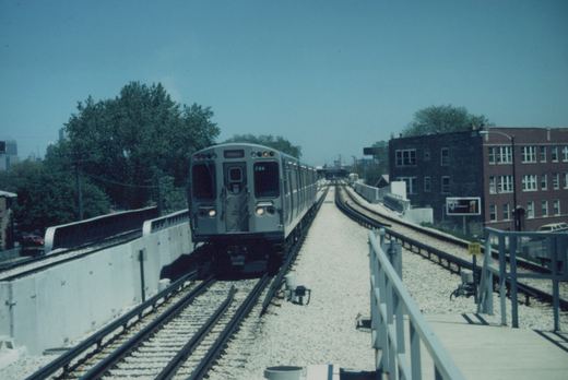 A silver and blue Chicago 'L' train, car 766, is shown approaching on elevated tracks with a clear blue sky and city buildings in the background.
