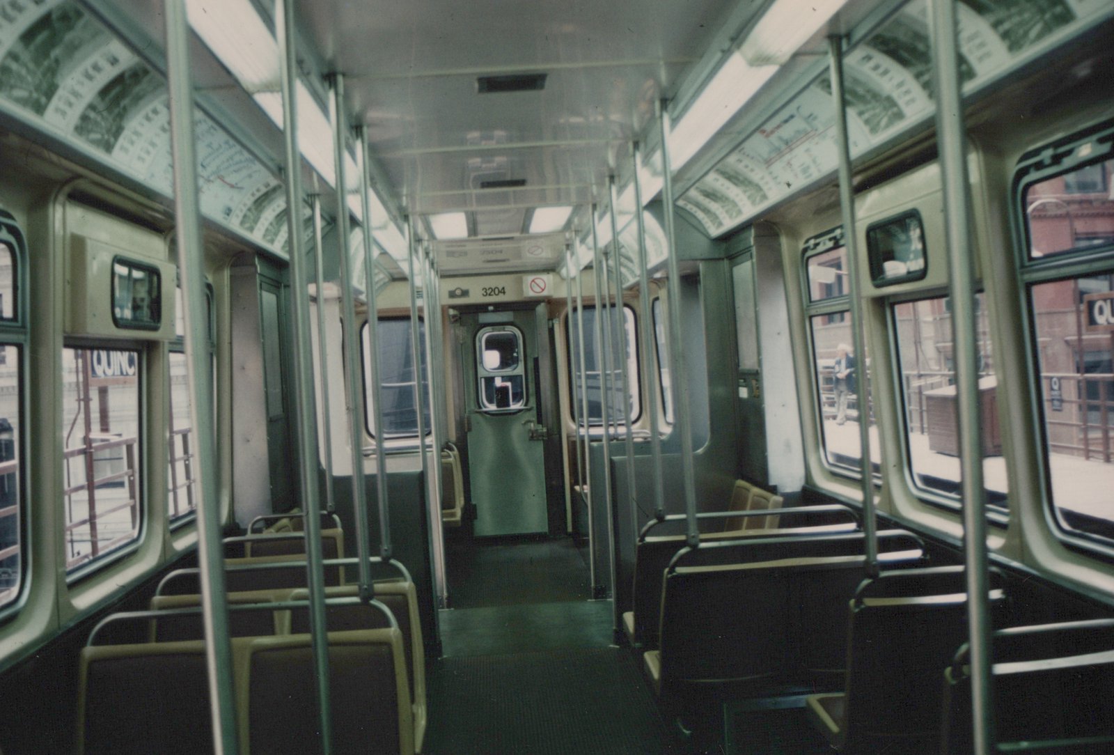 Interior view of a Chicago Transit Authority rapid transit car, number 3204, showing rows of seats, poles, and a door at the far end; through the windows, a station platform and a sign reading QUINC are visible.