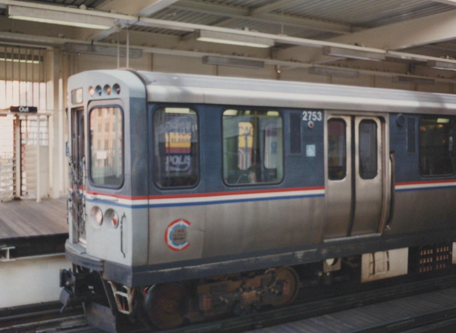 A blue and silver Chicago Transit Authority rapid transit car numbered 2753 is stopped at a station platform with a sign reading 'Out' visible in the background.