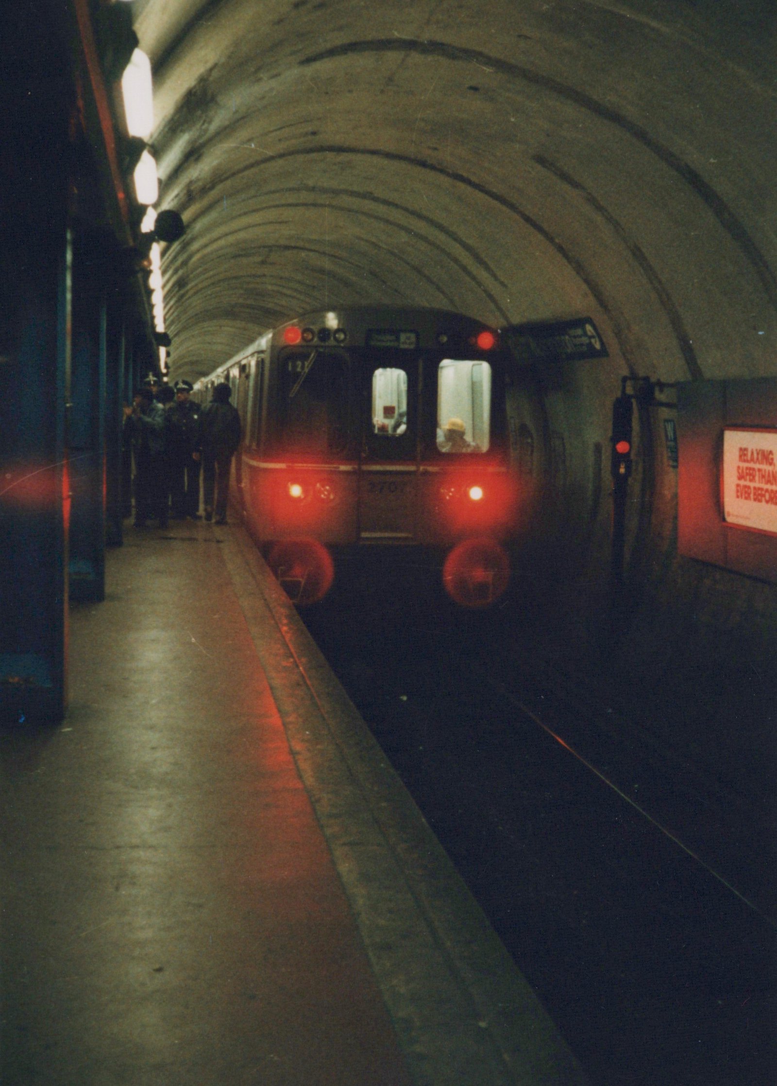 Front view of a CTA 2600 series train, number 2707, arriving at a station inside a curved concrete tunnel with passengers waiting on the platform.