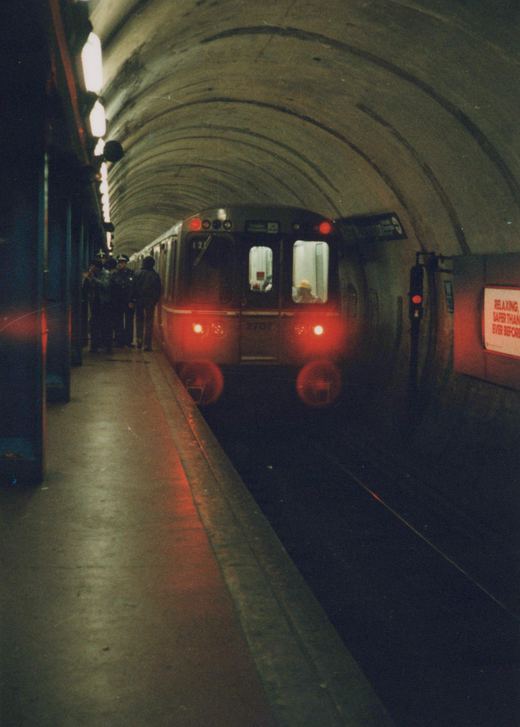 Front view of a CTA 2600 series train, number 2707, arriving at a station inside a curved concrete tunnel with passengers waiting on the platform.