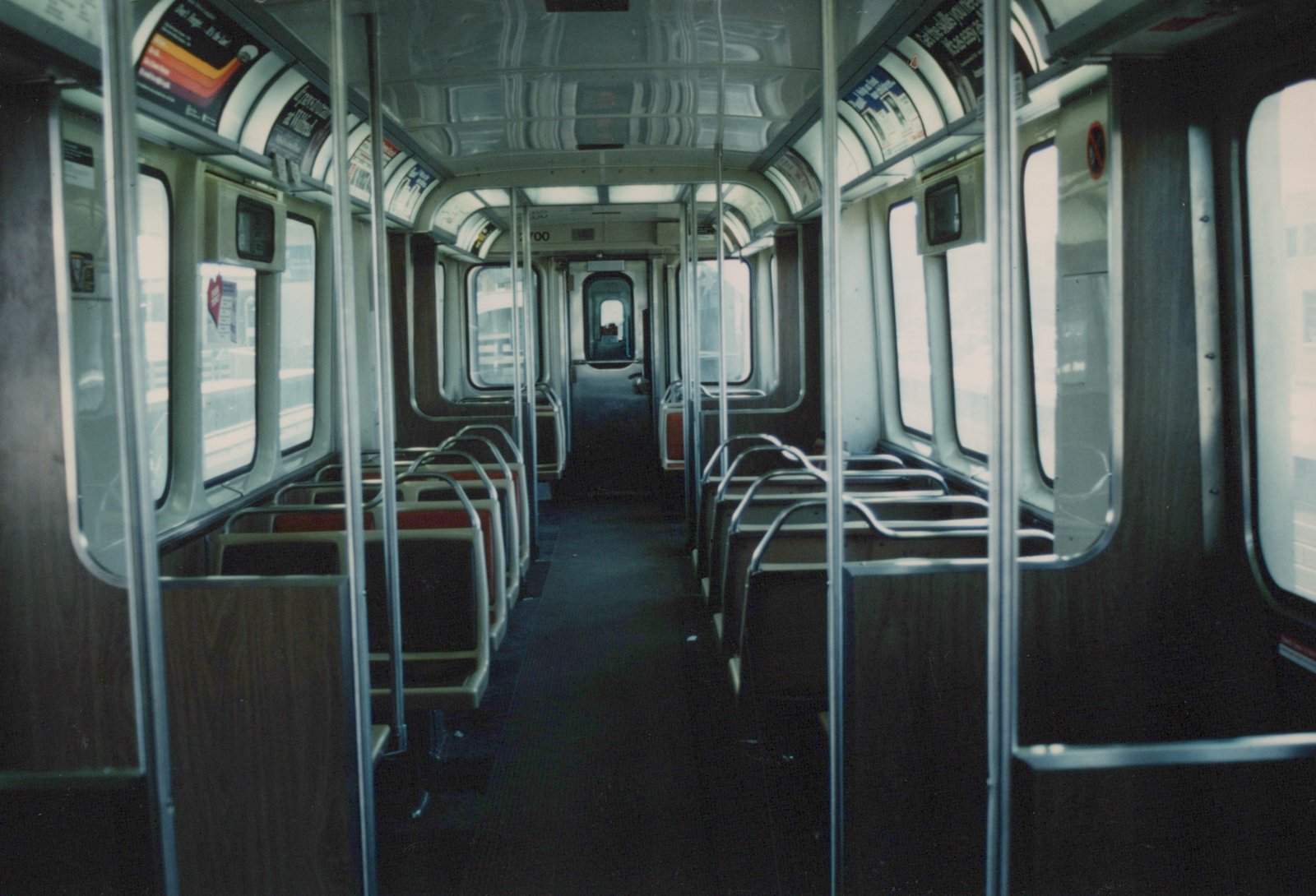 The empty interior of a CTA 'L' car, looking down the aisle toward the far end, with seats on both sides and vertical poles for standing passengers.