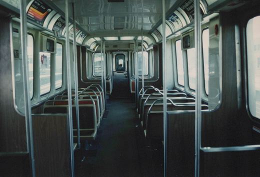 The empty interior of a CTA 'L' car, looking down the aisle toward the far end, with seats on both sides and vertical poles for standing passengers.