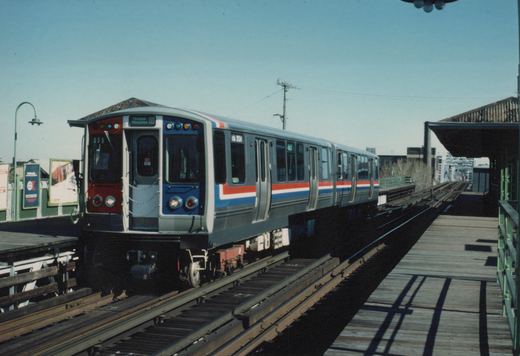 A silver CTA rapid transit train with red, white, and blue stripes, numbered 305, is stopped at an elevated station platform under a clear sky.