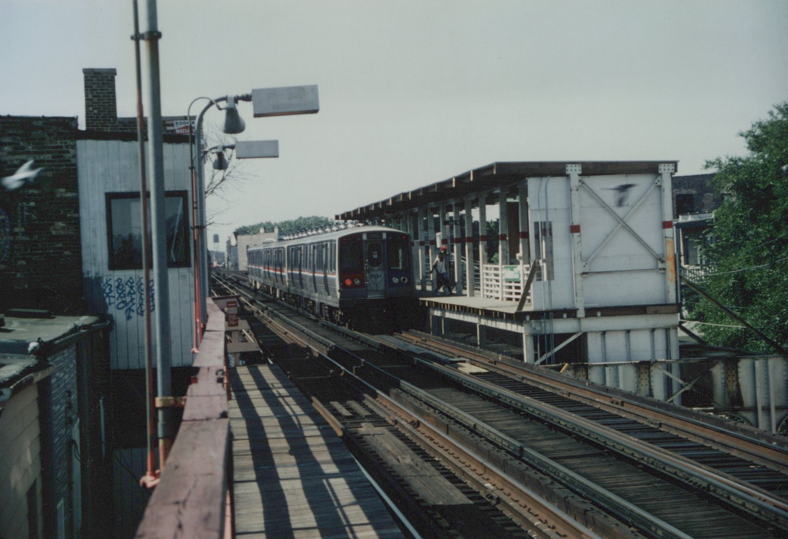 A silver and red train with the number 2691 on the front is moving on elevated tracks toward a platform with a person standing on it.