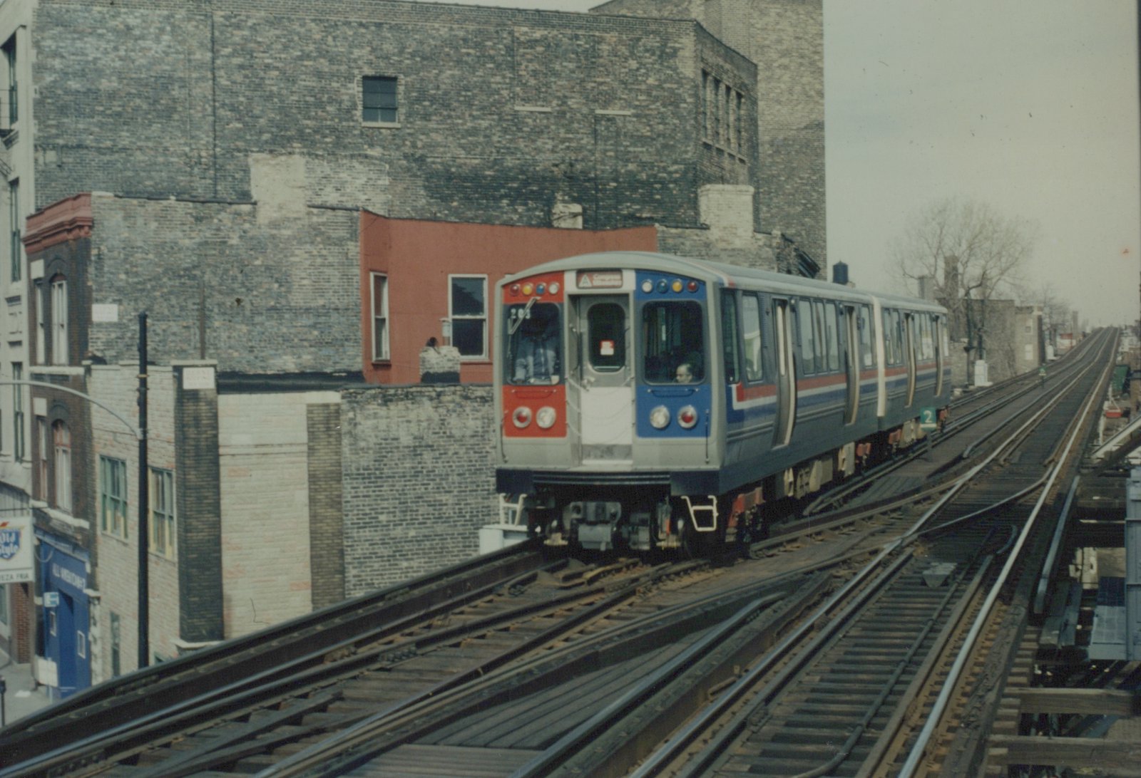 A blue, red and silver CTA train car marked 203 on elevated tracks next to brick buildings under an overcast sky.