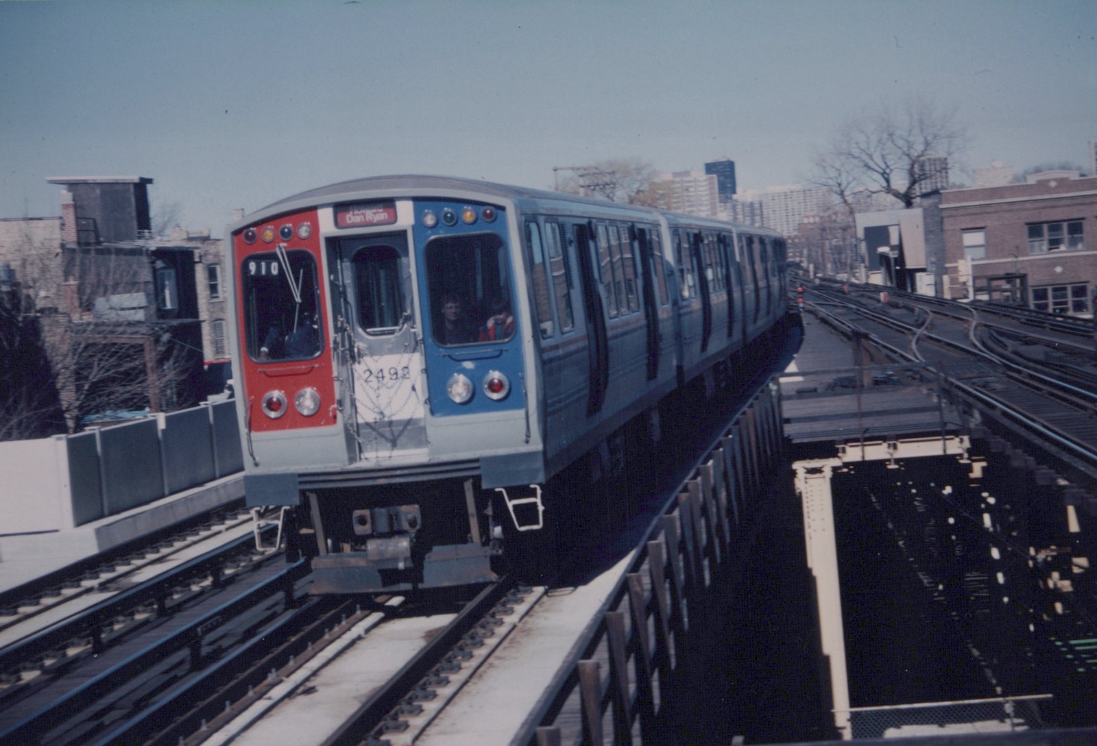 A Chicago 'L' train, numbered 2492, on an elevated track with a 'Dan Ryan' sign, under a clear sky with bare trees in the background.