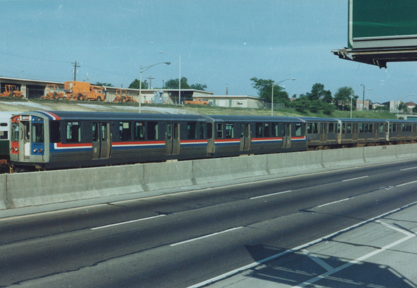 A side-view of a Chicago Transit Authority train, marked cta 2486, running on an elevated concrete structure above a highway, with construction equipment visible in the background.