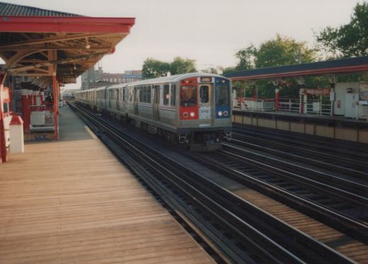 An elevated train with a silver, red, and blue front, marked 2476, is at a wooden-plank platform labeled Wellington station.