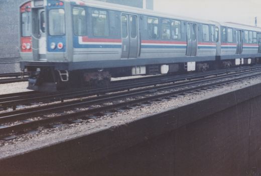A silver, blue and red rapid transit train, with the number 2453 visible on its side, is parked on elevated tracks against a gray, overcast sky.