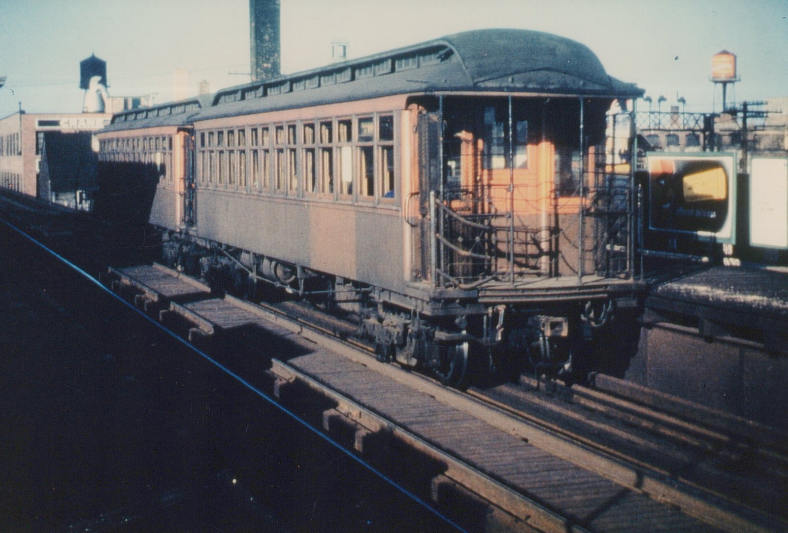 An early 20th-century interurban car with a cream and maroon livery and an open front platform is parked on an elevated wooden structure. Snow is visible on the platform and the car's roof.