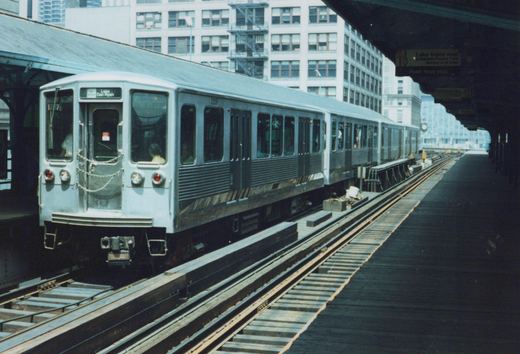 A silver CTA train car numbered 2208, displaying 'Lake Den Ryan' on its front, sits on an elevated track at a station platform with a large building in the background.