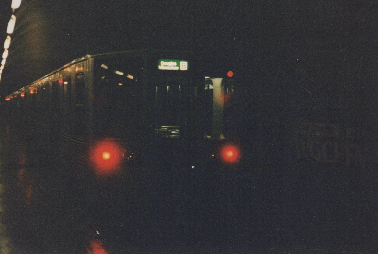 A dark rapid transit train with a green illuminated destination sign reading 'Douglas Milwaukee B' is visible in a subway tunnel at night.