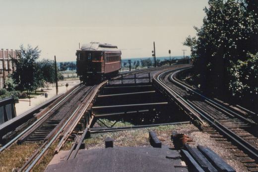 An old interurban railcar on elevated tracks with trees and water in the background.