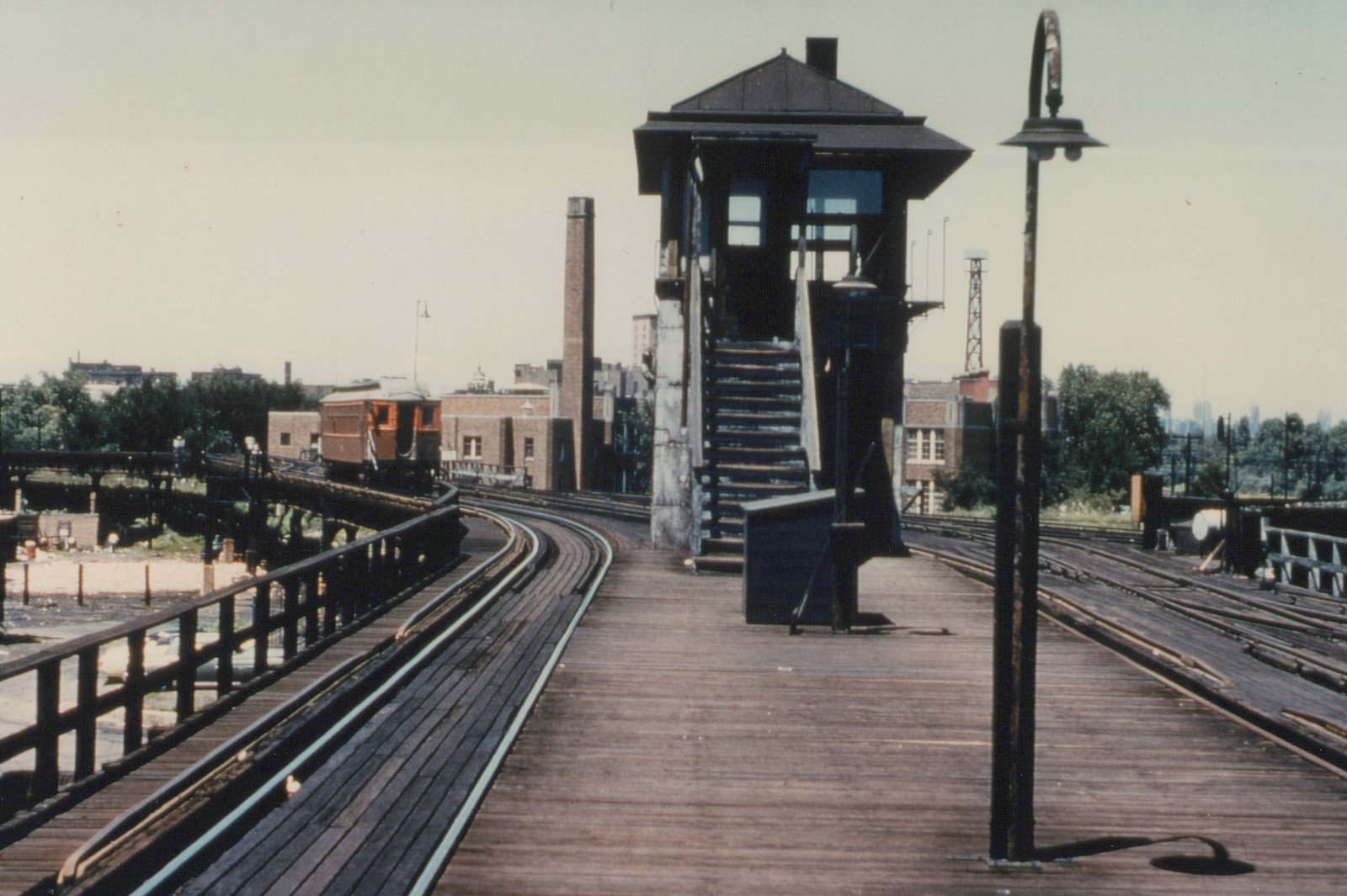 A maroon and cream rapid transit car on a wooden elevated track with a tower and brick buildings in the background.