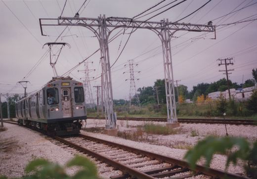 A silver Chicago Transit Authority rapid transit car, numbered 3441 and headed to Skokie, moves along tracks under a complex web of overhead wires on a cloudy autumn day.