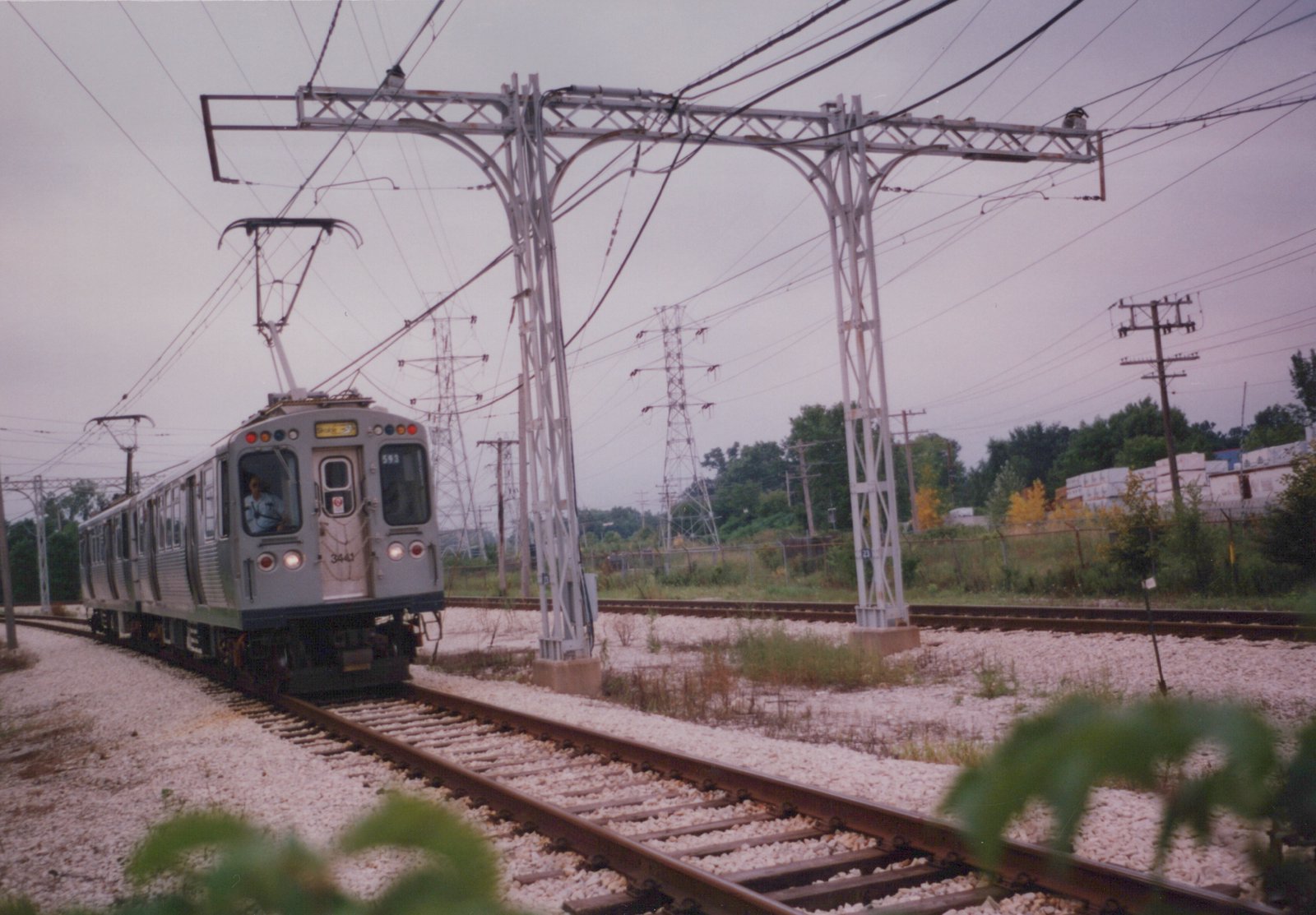 A silver Chicago Transit Authority rapid transit car, numbered 3441 and headed to Skokie, moves along tracks under a complex web of overhead wires on a cloudy autumn day.