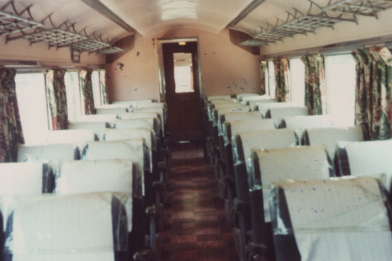 The interior of a passenger train car with rows of upholstered seats, a central aisle, and overhead luggage racks under a curved ceiling.