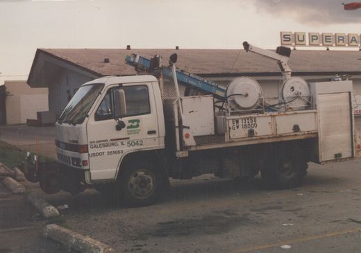 A white Isuzu utility truck with Burlington Northern lettering and fleet number 5042 is parked in front of a building with a 'SUPER A' sign.
