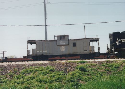 Side view of an Illinois Central gray caboose and a black locomotive on a railroad track with grass in the foreground.