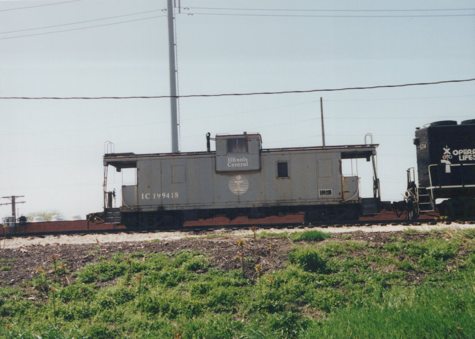 Side view of an Illinois Central gray caboose and a black locomotive on a railroad track with grass in the foreground.