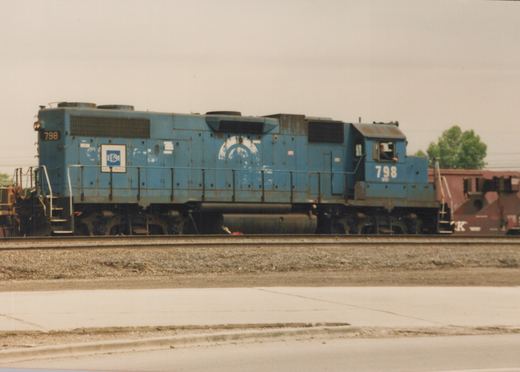 A blue diesel locomotive with the number 798 and E&M lettering is parked on railroad tracks in a yard with a freight car behind it.