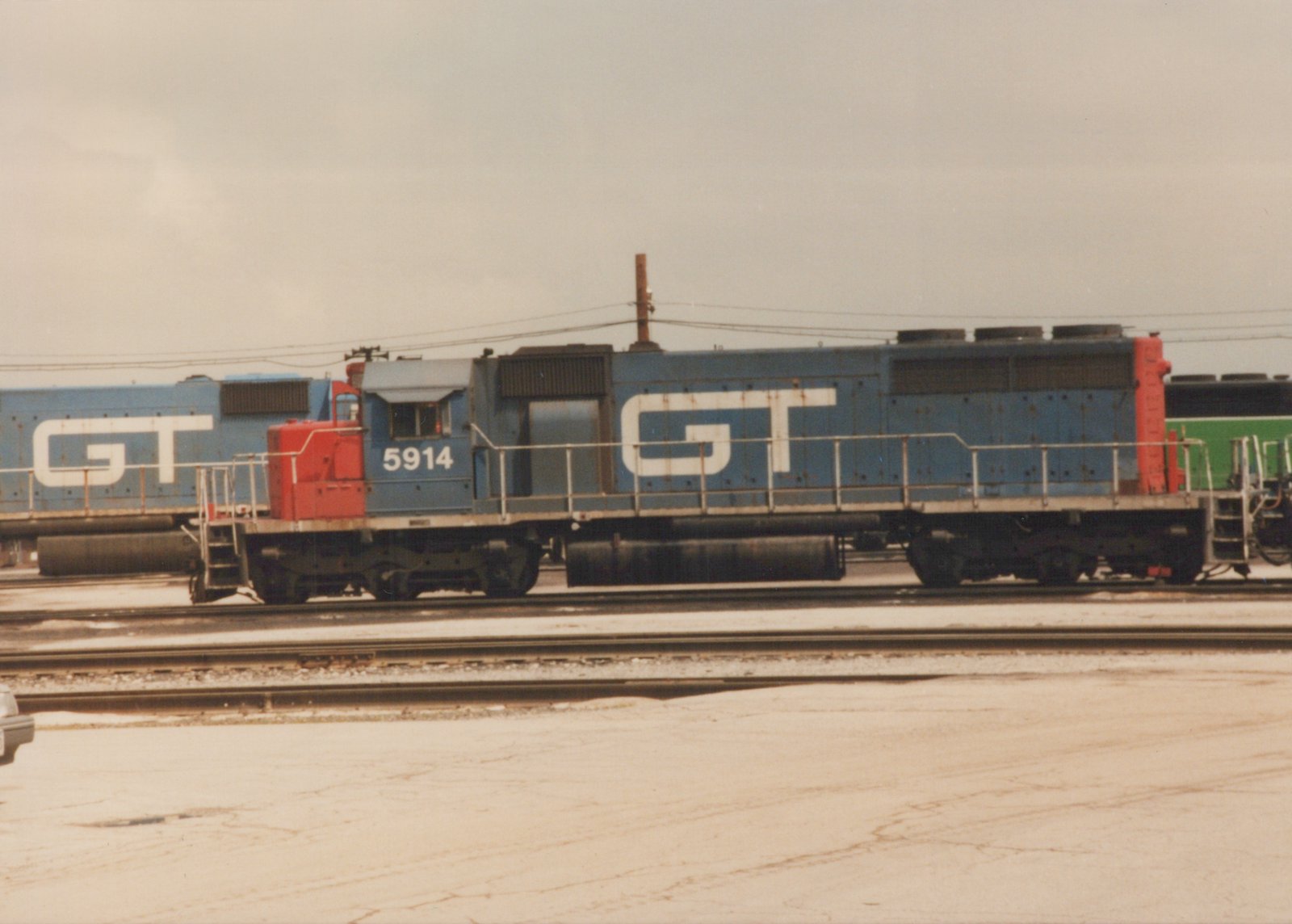 A blue and red Grand Trunk Western diesel locomotive, number 5914, is parked on railroad tracks in a yard on a cloudy day with snow on the ground.