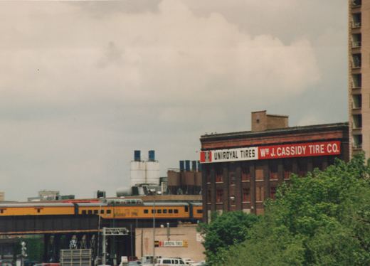 A Metra gallery car on an elevated track in Chicago, with the Wm J. Cassidy Tire Co. sign on a building behind it.