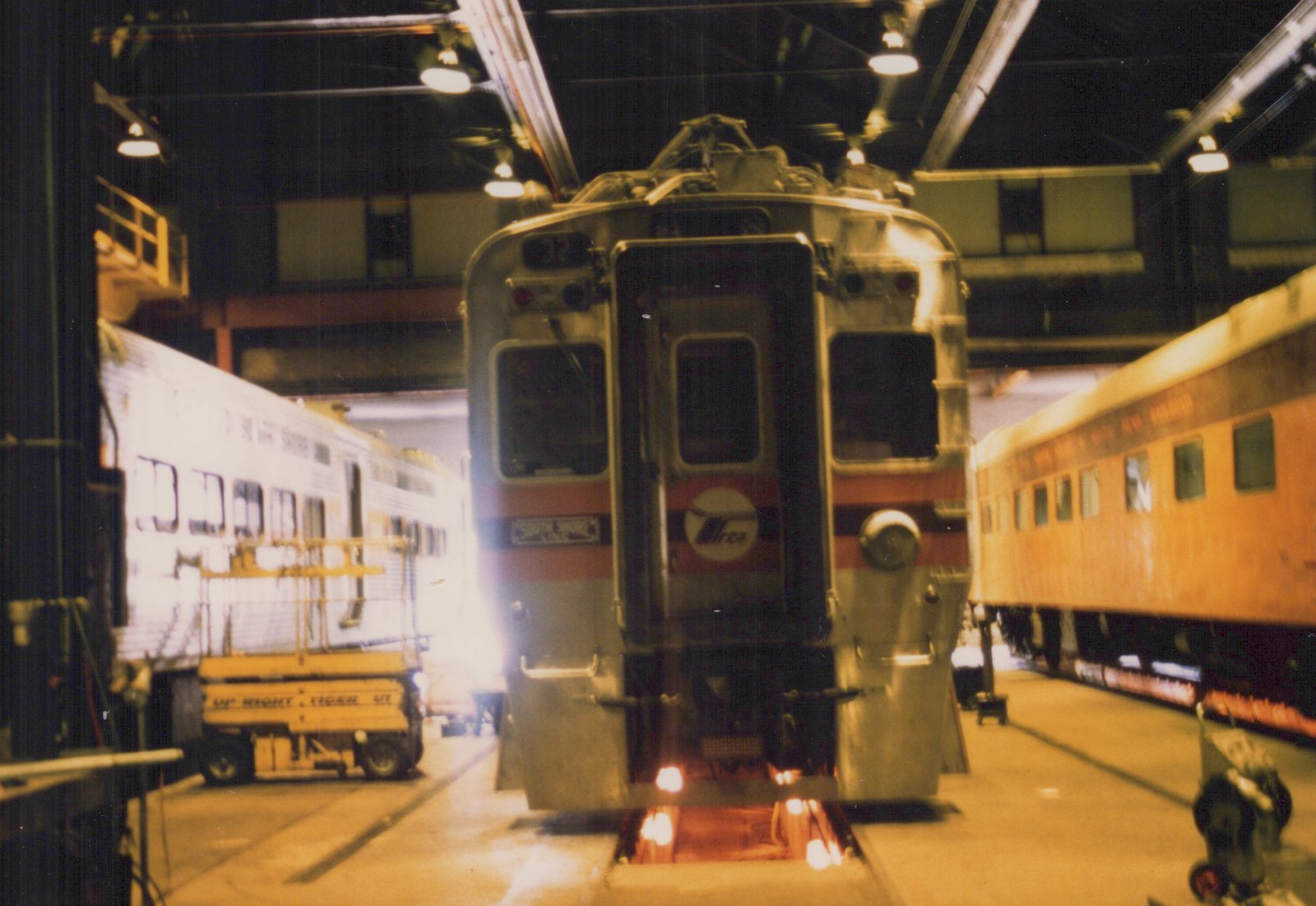 Front view of a South Shore Line electric train car, number 21, inside a rail shop with maintenance equipment and other cars nearby.