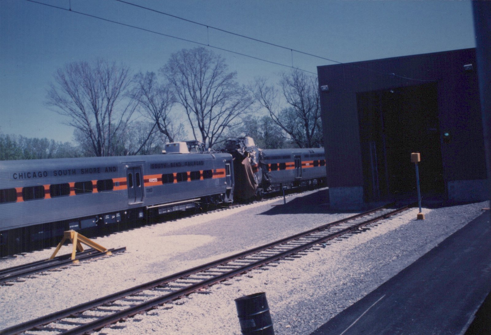 Two silver Chicago South Shore and South Bend Railroad Highliner cars, one with the number 1120, are coupled on a track in a yard under a clear sky with bare trees.