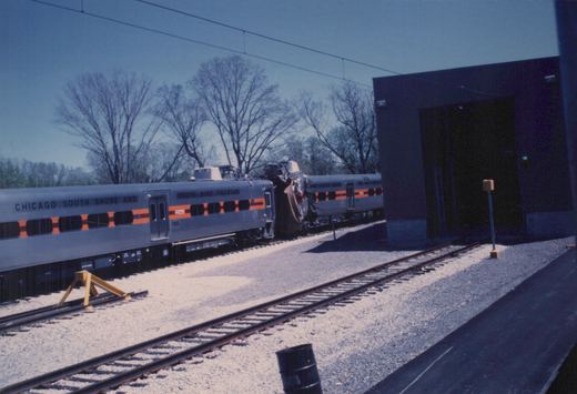 Two silver Chicago South Shore and South Bend Railroad Highliner cars, one with the number 1120, are coupled on a track in a yard under a clear sky with bare trees.
