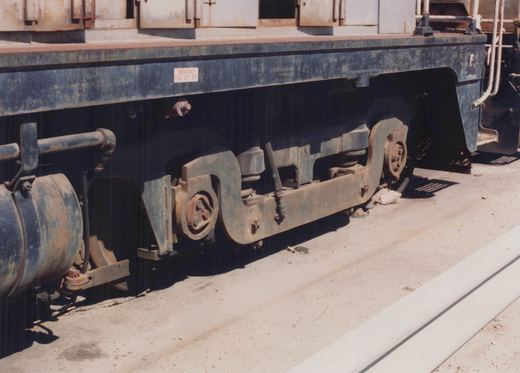 Side view close-up of a blue diesel locomotive's underframe and wheels on a concrete yard surface.